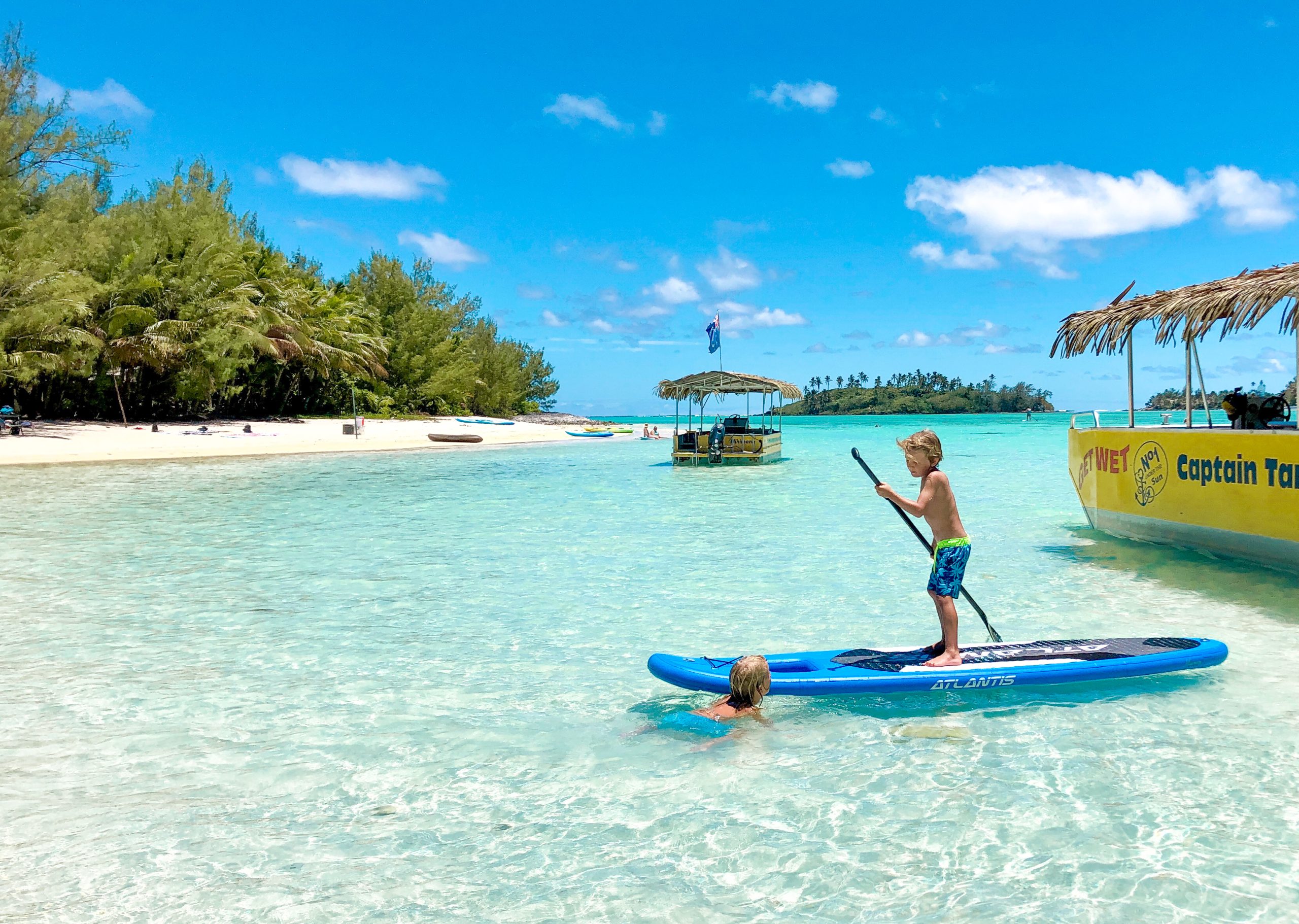 A boy on a SUP beside Captain Tama's Lagoon Cruise boat in Rarotonga