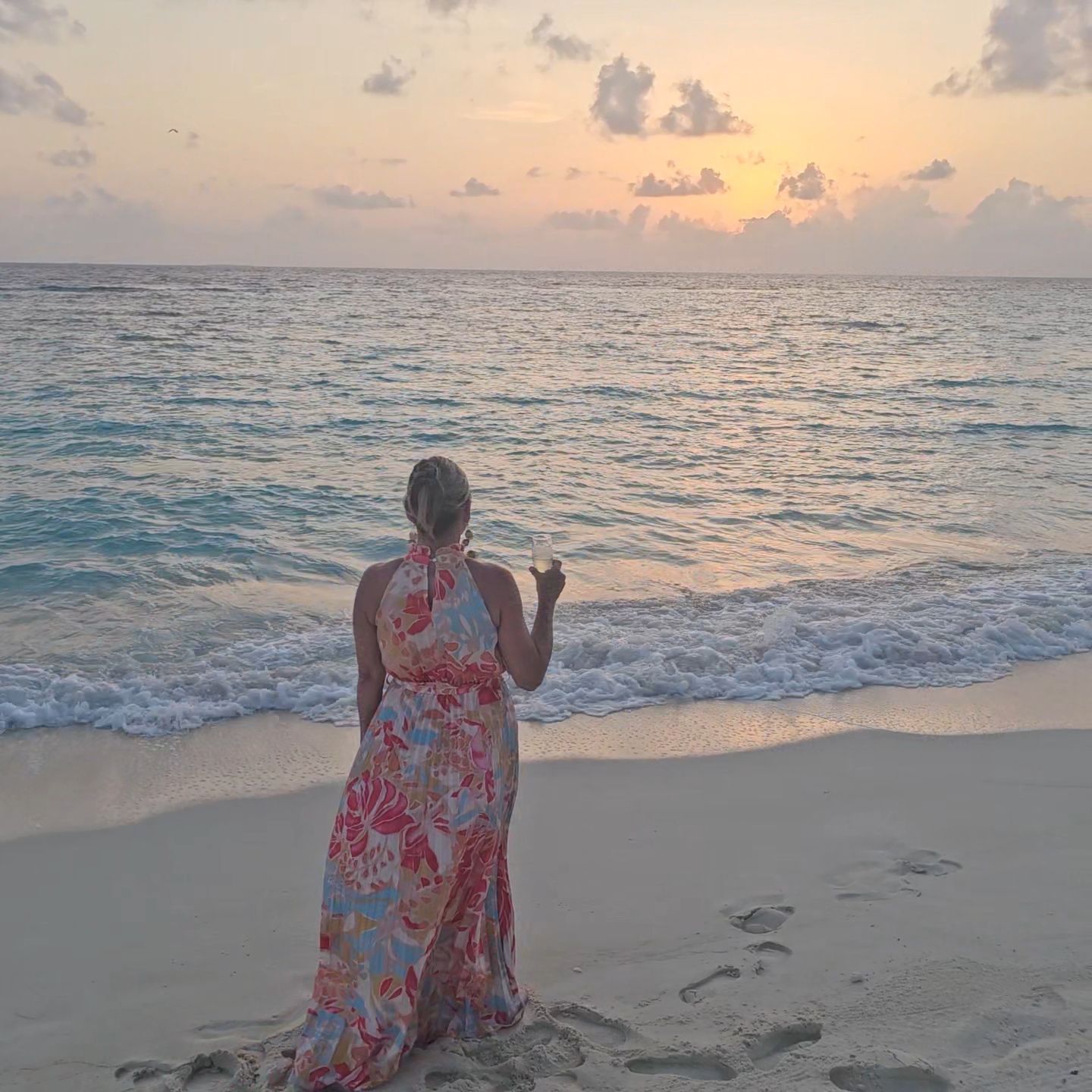 Woman standing on a Maldives beach at sunset, looking out over the ocean