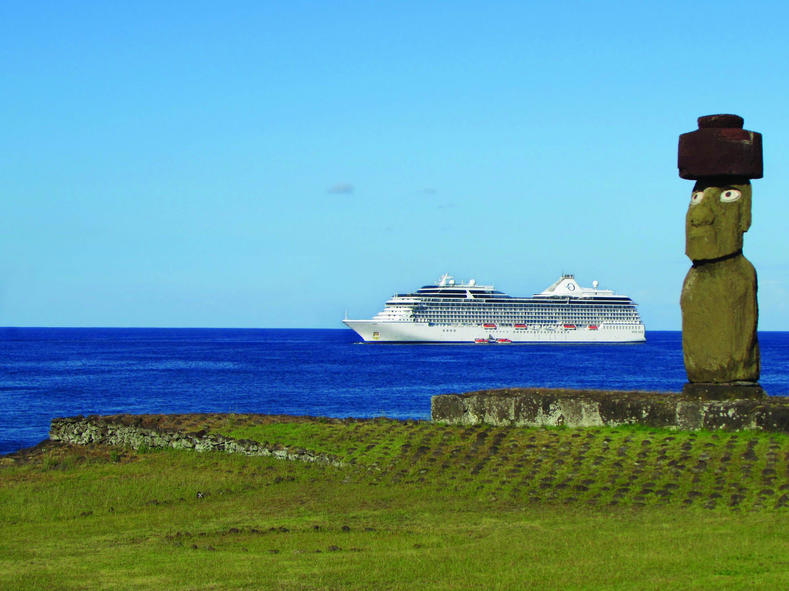 Luxury cruise ship sailing past Easter Island with Moai statue in the foreground