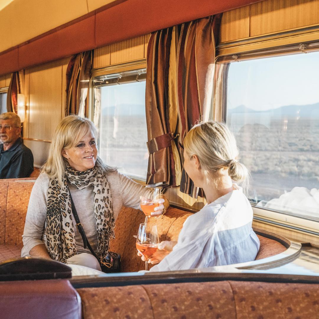 Two guests enjoying drinks in the Gold Service Lounge aboard The Ghan