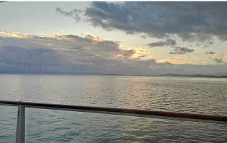 Sunset over the water viewed from a cruise ship balcony, with the railing in the foreground