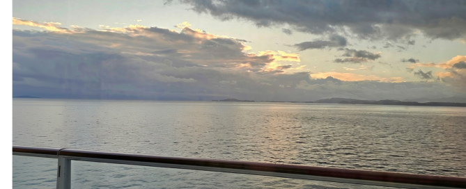 Sunset over the water viewed from a cruise ship balcony, with the railing in the foreground